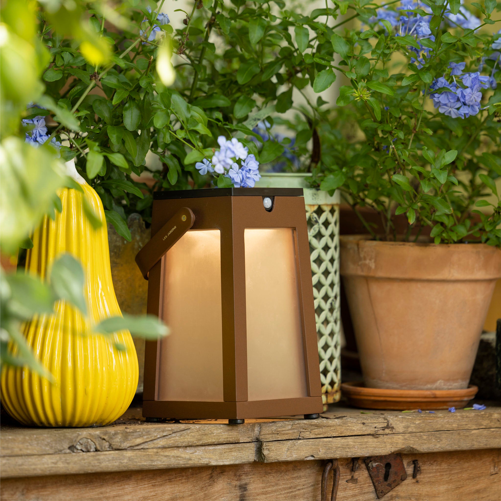 Tinka solar lantern corten finish among potted plants